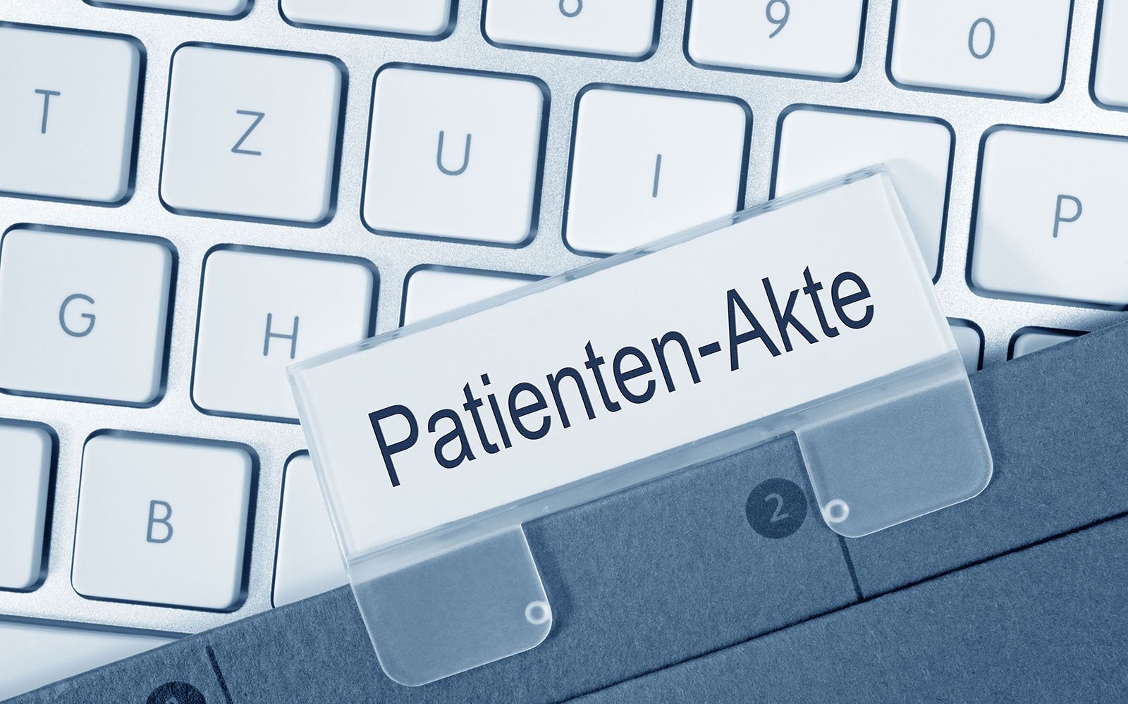 Der Ausschnitt einer weißen Tastatur, auf der eine graue Patientenakte liegt.